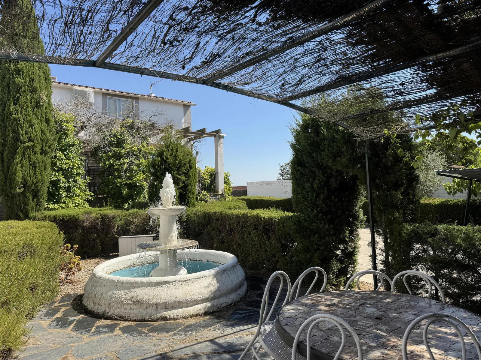 Jardín con fuente de piedra y mesa a la sombra de la pérgola